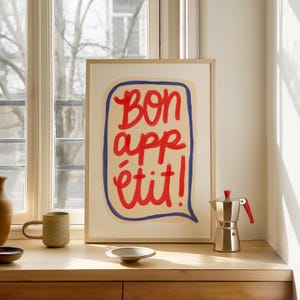 Peut inclure: Une affiche encadrée avec un fond blanc et une bulle de dialogue bleue et rouge qui dit "Bon appétit!" en lettres rouges.