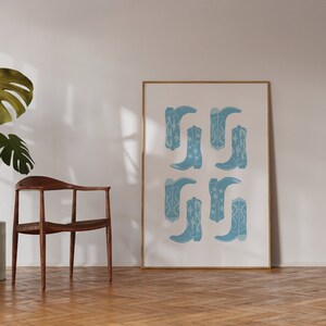 May include: A framed print with a white background and a pattern of blue cowboy boots with white stars and cactus designs.