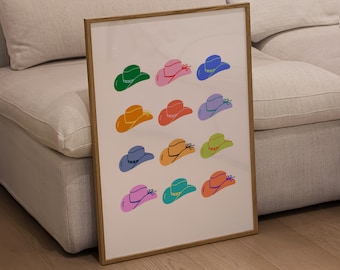 May include: A framed art print featuring a pattern of colorful cowboy hats. The hats are in various colors, including green, pink, blue, orange, red, and purple. The print is displayed on a white background and framed in a light brown wooden frame.