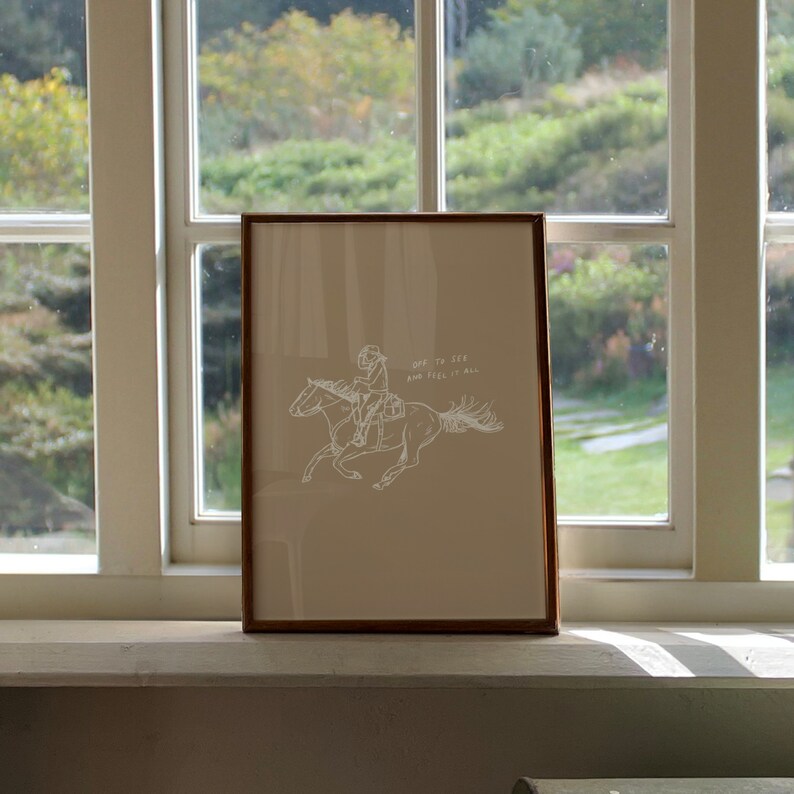 Pu&ograve; includere: Una stampa incorniciata con un disegno a linea bianca di una persona a cavallo. Il testo "Off to see and feel it all" &egrave; sotto l'immagine.