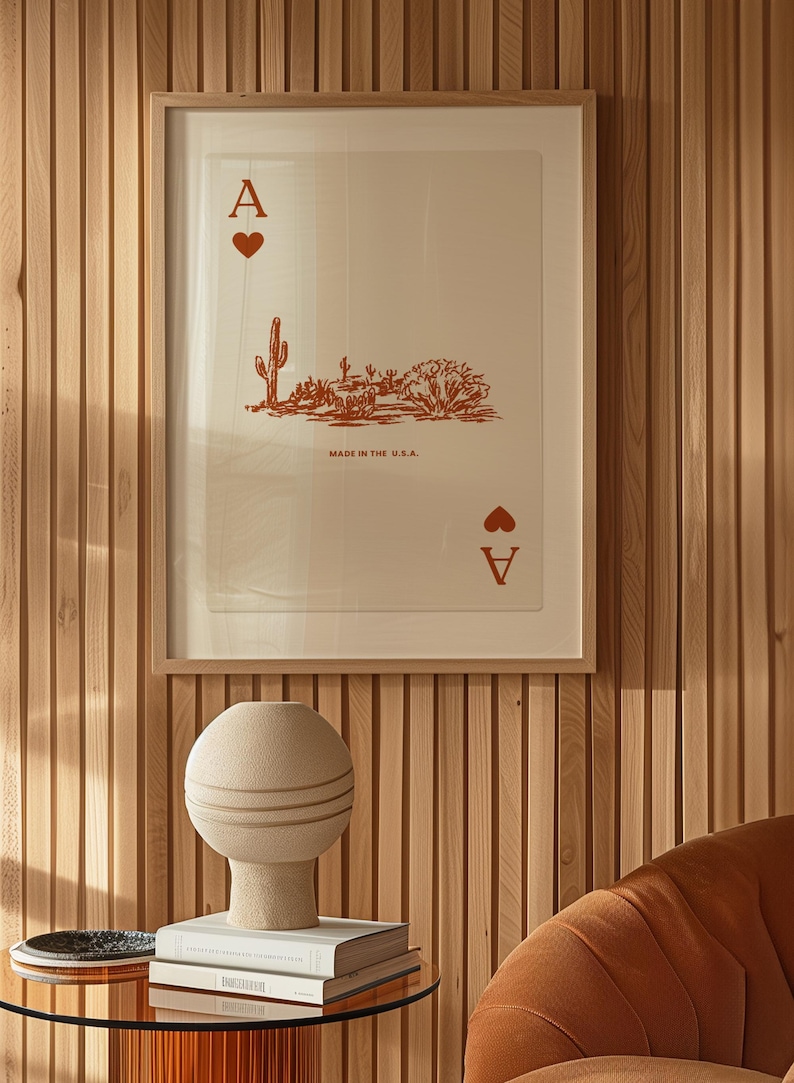 May include: A framed print of an ace of spades playing card with a desert landscape illustration. The card is printed in red on a white background with the text "Made in the U.S.A.". The print is hanging on a wood panel wall.