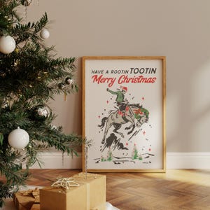 Puede incluir: Un estampado enmarcado con tem&aacute;tica navide&ntilde;a. La obra de arte presenta a un vaquero montando un caballo salvaje, con el texto "Have a Rootin' Tootin' Merry Christmas". La ilustraci&oacute;n es en tonos grises, verdes y rojos.