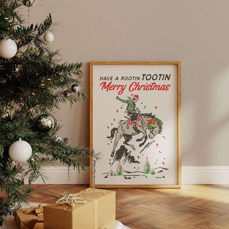 Puede incluir: Un estampado enmarcado con tem&aacute;tica navide&ntilde;a. La obra de arte presenta a un vaquero montando un caballo salvaje, con el texto "Have a Rootin' Tootin' Merry Christmas". La ilustraci&oacute;n es en tonos grises, verdes y rojos.