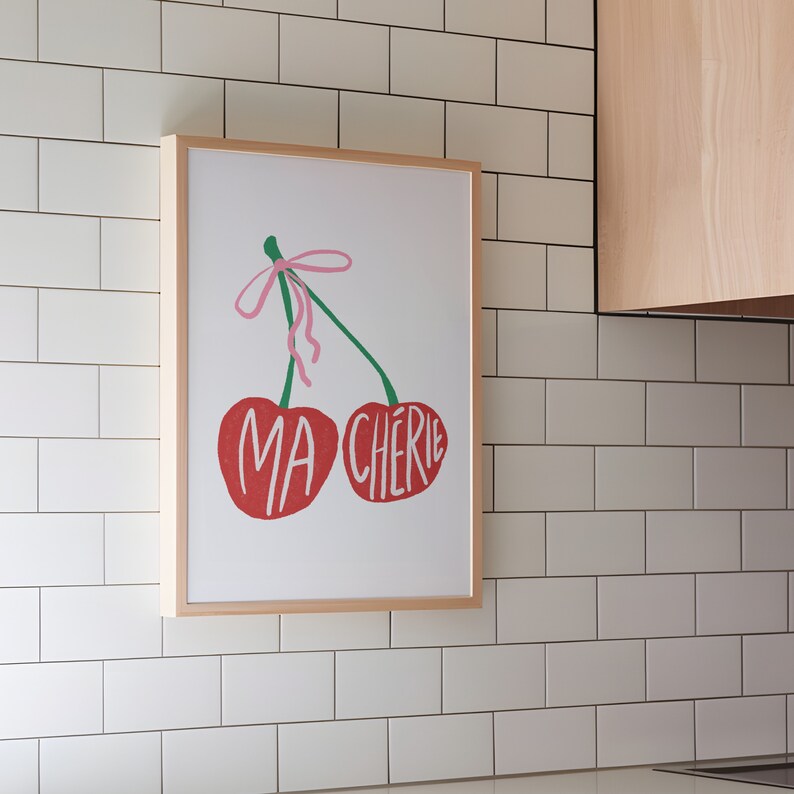 May include: A framed print of two red cherries with green stems and a pink bow. The cherries are labeled "MA CHERIE" in white text.
