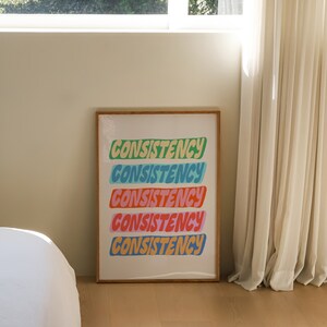 May include: A framed print with the word "CONSISTENCY" repeated five times in a colorful, stylized font. Each word is a different color: green, blue, light blue, pink, and yellow.