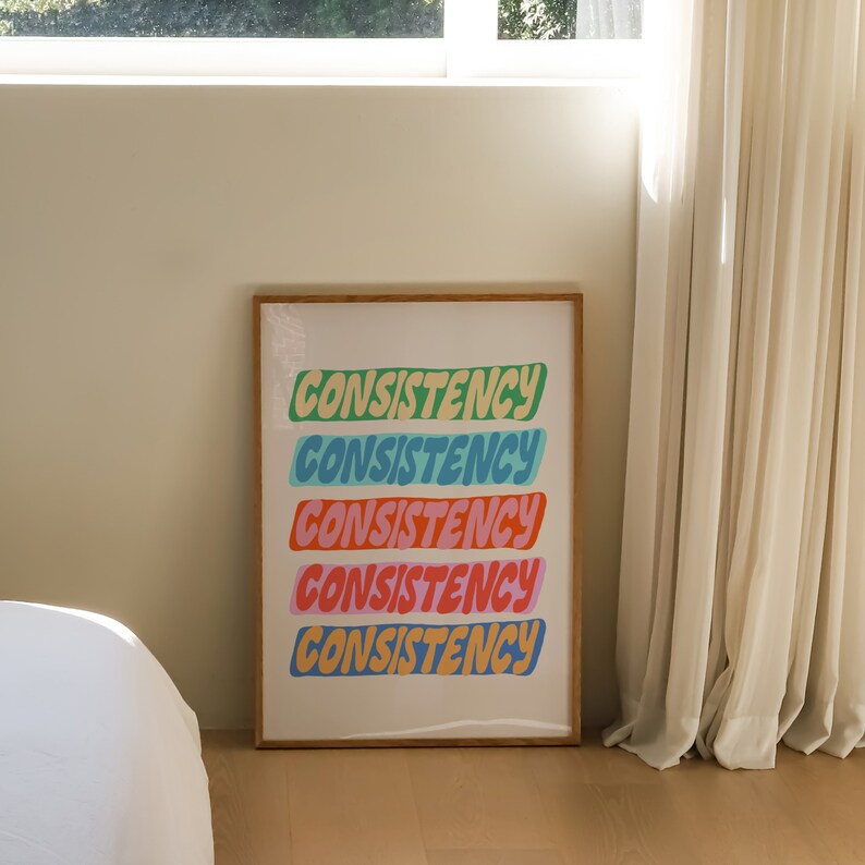 May include: A framed print with the word "CONSISTENCY" repeated five times in a colorful, stylized font. Each word is a different color: green, blue, light blue, pink, and yellow.