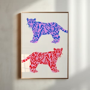 Op de afbeelding: Een ingelijst drukwerk met twee gestileerde illustraties van luipaarden. De bovenste luipaard is roze met blauwe vlekken en de onderste luipaard is roze met rode vlekken.