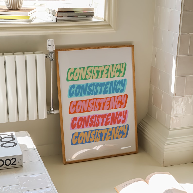 May include: A framed print with the word "CONSISTENCY" repeated five times in a colorful, bubbly font. Each word is a different color: green, blue, orange, pink, and blue.