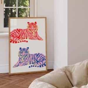 May include: A framed print featuring two stylised tigers, one in pink and red with black stripes, and the other in pink and blue with black stripes. Both tigers are lying down and facing forward.