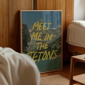May include: A framed print with a mountain landscape and the text "MEET ME IN THE TETONS" in yellow lettering.