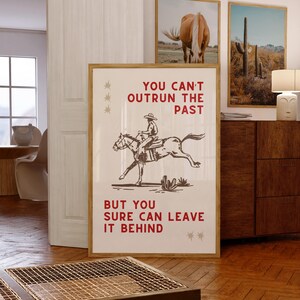 Könnte beinhalten: Ein Vintage-Poster mit einem Cowboy, der auf einem Pferd reitet. Das Poster hat einen weißen Hintergrund mit rotem Text, der lautet "You can't outrun the past but you sure can leave it behind."