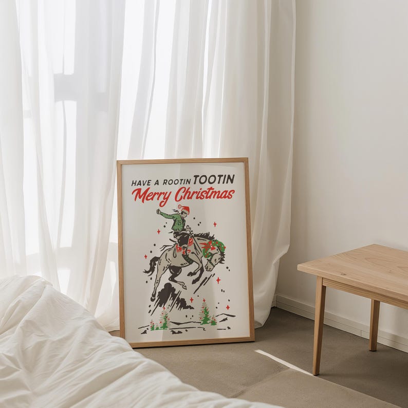Puede incluir: Un estampado enmarcado con tem&aacute;tica navide&ntilde;a. La obra de arte presenta a un vaquero montando un caballo salvaje, con el texto "Have a Rootin Tootin Merry Christmas" en rojo y verde. El estampado est&aacute; en un marco de madera.