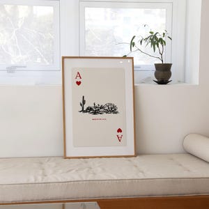 Op de afbeelding: Een ingelijste print van de aas van harten speelkaart met een woestijnsc&egrave;ne in zwart-wit. De kaart is ingelijst in een licht houten lijst. De tekst "Made in the U.S.A." is op de kaart gedrukt.