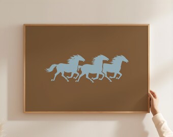 May include: A framed artwork featuring three light blue horse silhouettes galloping across a brown background. The artwork is encased in a natural wood frame, creating a simple yet elegant aesthetic. The image is displayed on a white wall.