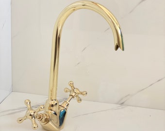 May include: A gold-toned kitchen faucet with a high arc spout and two cross-shaped handles.