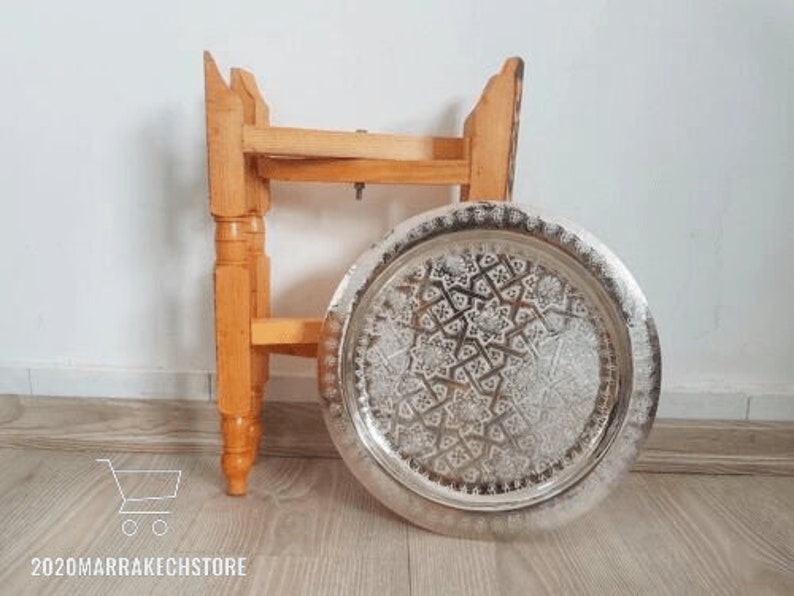 May include: A wooden stand with a round, silver tray. The tray has an intricate, embossed design.