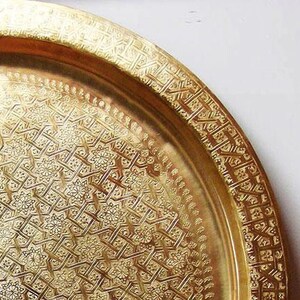 May include: A large, round, gold-colored metal serving tray with an intricate, embossed geometric pattern.