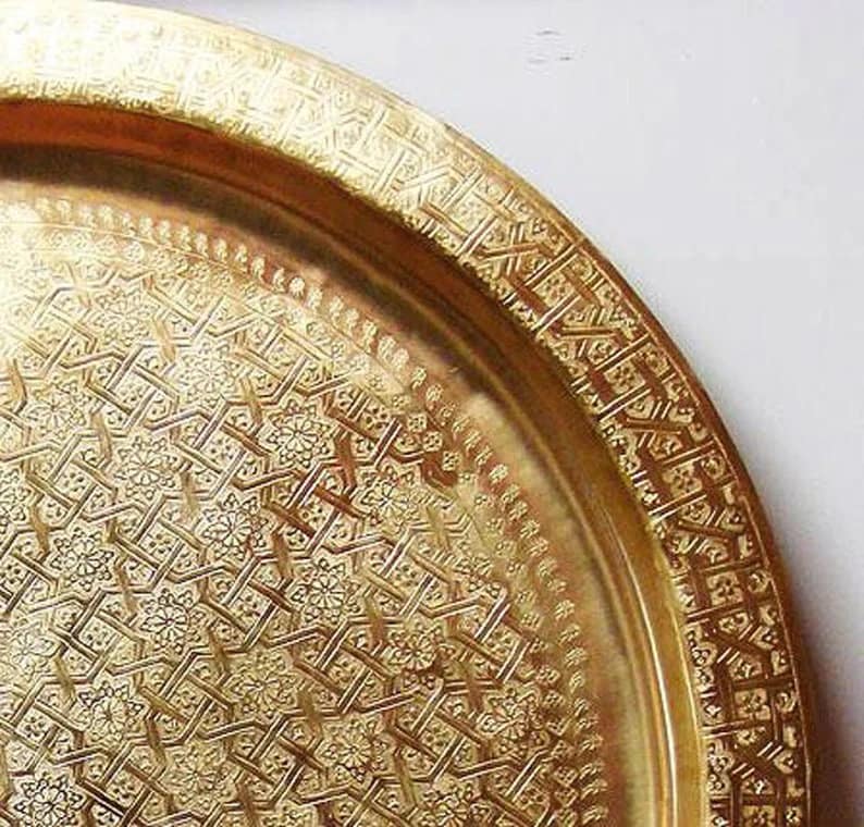 May include: A large, round, gold-colored metal serving tray with an intricate, embossed geometric pattern.