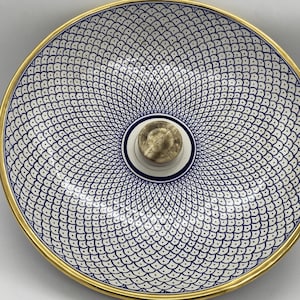 May include: Decorative ceramic bowl with a white and blue fish scale pattern. The bowl has a gold rim and a brass-colored knob in the center. The bowl is a decorative piece.