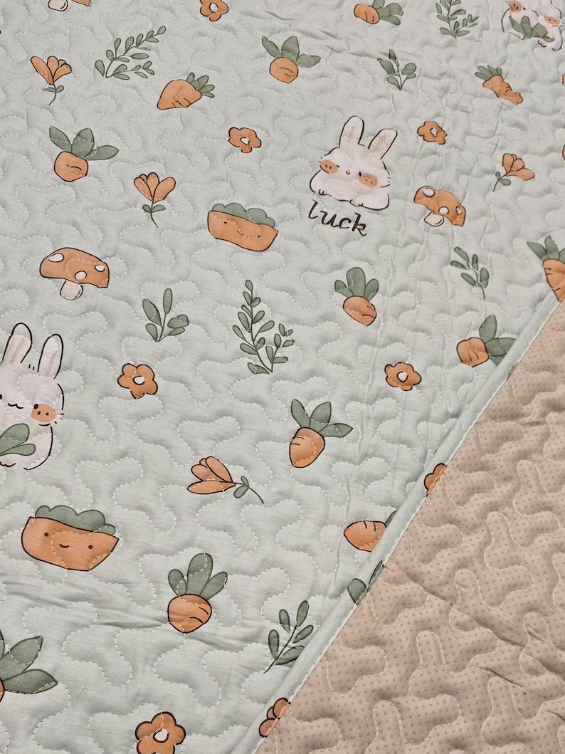 May include: A light green quilted fabric with a repeating pattern of cartoon bunnies, carrots, mushrooms, and flowers. The word "luck" is written near a bunny. The fabric has a wavy, stitched design.