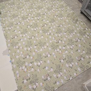 May include: A large, rectangular, quilted play mat with a light green background. The mat features a repeating pattern of cartoon bunnies, trees, and carrots. The mat is designed for babies and toddlers.