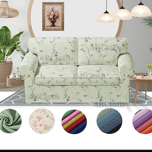 以下が含まれることがあります： 薄い緑色の花柄のソファで、明るい木製のフレームが付いています。 ソファはグレーと白の模様の敷物の上に置かれています。 ソファの下には、さまざまな色と模様のファブリック見本が5つあります。