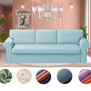May include: A light blue sofa with three cushions and a tufted back. The sofa is in a room with a pink wall and a chandelier. The sofa is available in a variety of fabrics, including floral, solid, and textured.