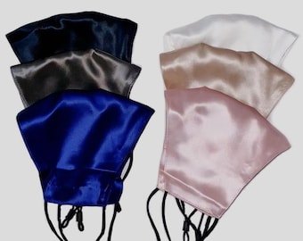 Op de afbeelding: Een verzameling satijnen gezichtsmaskers in diverse kleuren, waaronder marineblauw, grijs en roze. Elk masker heeft verstelbare zwarte oorlussen voor een comfortabele pasvorm. De maskers zijn in twee groepen gerangschikt, waarbij de verschillende kleuropties worden getoond.
