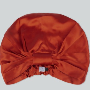 Pode incluir: Um turbante de cabelo de cetim cor de ferrugem com um laço na parte superior. O turbante é projetado para proteger o cabelo durante o sono.