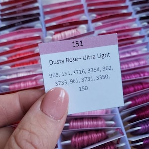 May include: A close-up of a pink and white label with the text "151 Dusty Rose- Ultra Light" and a list of DMC floss numbers: 963, 151, 3716, 3354, 962, 3733, 961, 3731, 3350, 150.