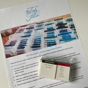 May include: A white sheet of paper with instructions on how to organize embroidery floss by color family. The paper includes the text "The Tidy Stitch - Family Organization System". There are also color-coded cards with floss numbers and names.