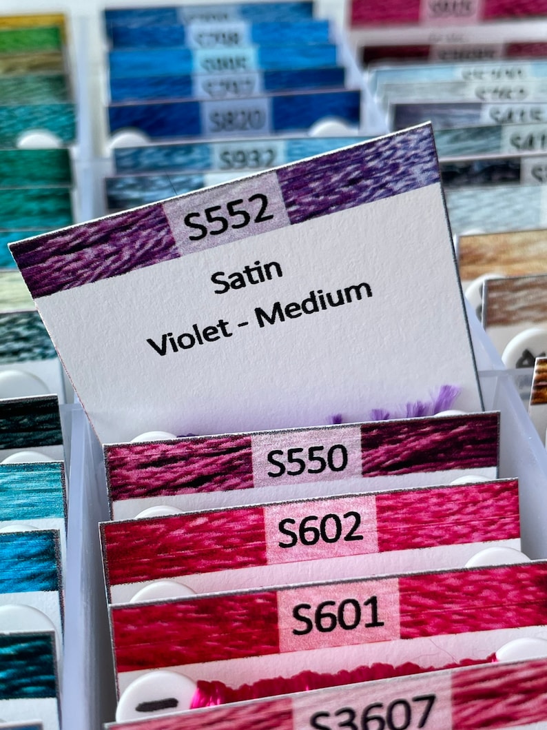 May include: A close-up of a collection of embroidery floss spools, with a label for spool number S552, Satin Violet - Medium.