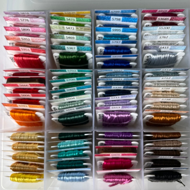 May include: A close-up of a plastic storage box filled with rows of colorful embroidery floss spools. Each spool is labeled with a number and a color code. The floss is organized by color and number.