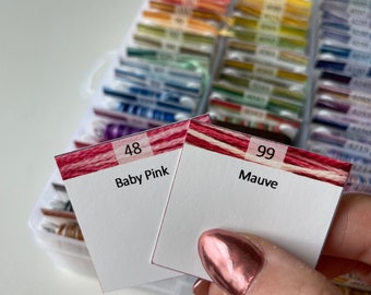 May include: Two embroidery floss cards with red and white stripes. The card on the left is labeled "48 Baby Pink" and the card on the right is labeled "99 Mauve".