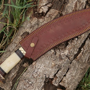 May include: A brown leather sheath with a decorative stitch pattern and a brass button. The sheath is wrapped around a knife with a white bone handle and a dark wood accent.
