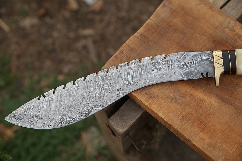 May include: A curved, silver-colored knife with a serrated edge and a patterned blade. The handle is made of wood and bone with a brass accent.
