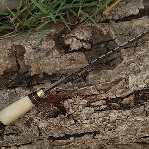 May include: A white-handled knife with a brown and gold accent on the handle. The blade is serrated and has a dark finish.