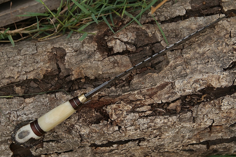 May include: A white-handled knife with a brown and gold accent on the handle. The blade is serrated and has a dark finish.