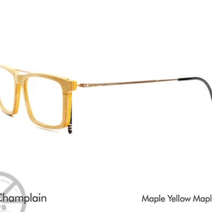 K&ouml;nnte beinhalten: Eine Brille aus Holz mit einem braunen Metallrahmen und schwarzen B&uuml;gelenden. Der Rahmen ist aus Ahornholz gefertigt und hat eine gelbe Ahorn-Oberfl&auml;che. Die Brille hei&szlig;t "Champlain".