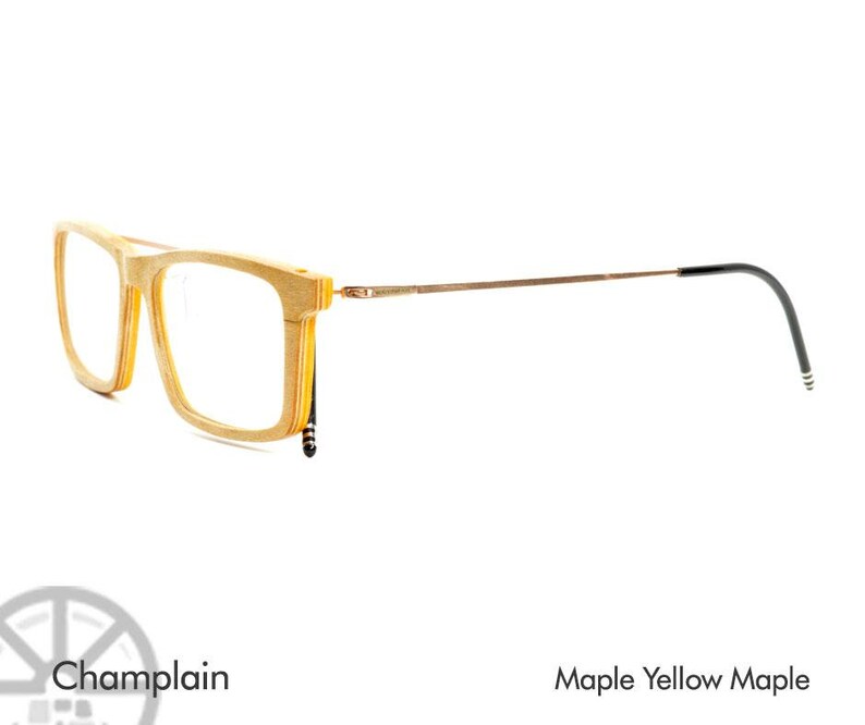 K&ouml;nnte beinhalten: Eine Brille aus Holz mit einem braunen Metallrahmen und schwarzen B&uuml;gelenden. Der Rahmen ist aus Ahornholz gefertigt und hat eine gelbe Ahorn-Oberfl&auml;che. Die Brille hei&szlig;t "Champlain".