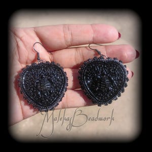 May include: A pair of heart-shaped earrings featuring black beadwork and a central black turtle motif. The earrings are constructed with small, dark, reflective beads arranged in a dense pattern, finished with black metal earring hooks.