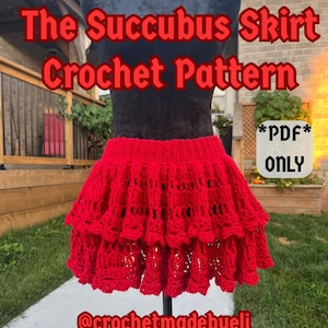 Puede incluir: Una falda roja de ganchillo con un diseño escalonado se muestra en un maniquí negro. El texto "The Succubus Skirt Crochet Pattern" está en rojo, junto con "*PDF* ONLY" y el identificador de Instagram "@crochetmadebyeli".