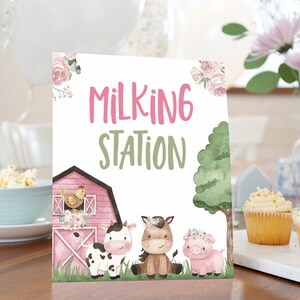 Może przedstawiać: Różowo-biały znak z napisem "Milking Station" w różowych i zielonych literach. Znak przedstawia kreskówkowy obórkę, krowę, konia i świnię.