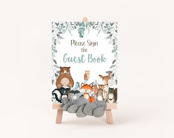 May include: A white sign with a green leafy border and the text "Please Sign the Guest Book".  The sign features a watercolor illustration of a bear, owl, fox, deer, raccoon, and squirrel.