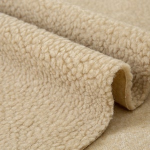 May include: Close-up of a beige faux fur fabric with a soft, fuzzy texture. The fabric is folded over itself, revealing a smooth, brown underside.