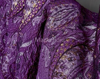 May include: Close-up of a textured purple fabric with a paisley design and gold accents. The fabric has a crinkled appearance and a sheen. The word "Mackendia" is visible on the fabric. The overall theme is textiles.