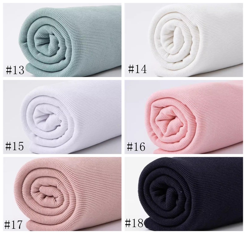 Op de afbeelding: Close-up van zes rollen geribbelde stof in verschillende kleuren: lichtblauw, wit, roze, lichtroze en zwart. De stof is opgerold en de uiteinden zijn zichtbaar. De nummers #13, #14, #15, #16, #17 en #18 zijn onder elke rol afgedrukt.