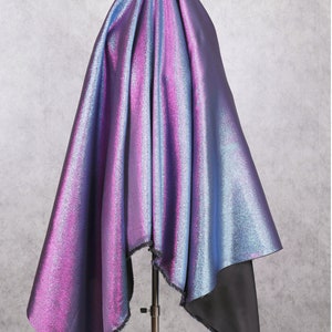 Può includere: Un pezzo di tessuto iridescente con un gradiente di colore blu e viola. Il tessuto è drappeggiato su un supporto e ha un bordo sfrangiato.