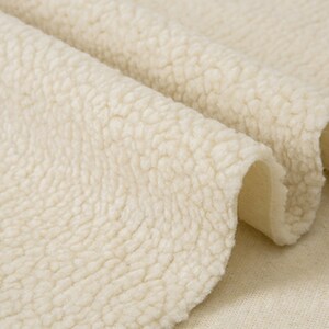 May include: Close-up of a soft, cream-colored, fluffy fabric with a textured surface. The fabric is folded in half, revealing a smooth, white underside.