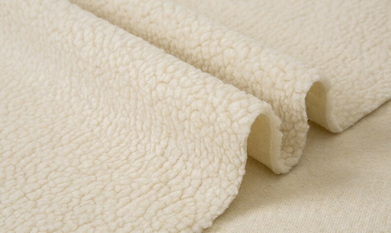 May include: Close-up of a soft, cream-colored, fluffy fabric with a textured surface. The fabric is folded in half, revealing a smooth, white underside.